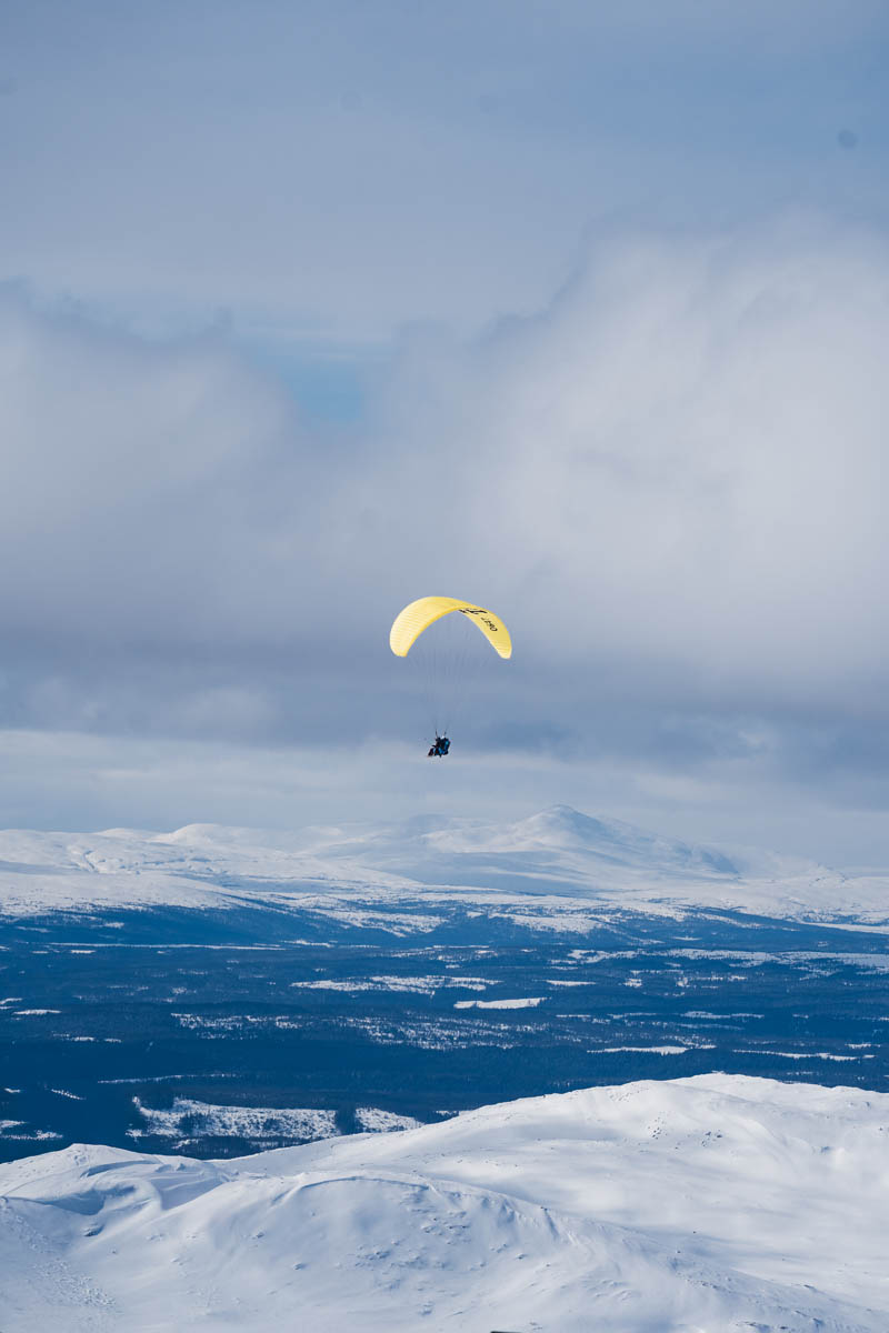 Paraglider över snötäckt fjäll under molnig himmel