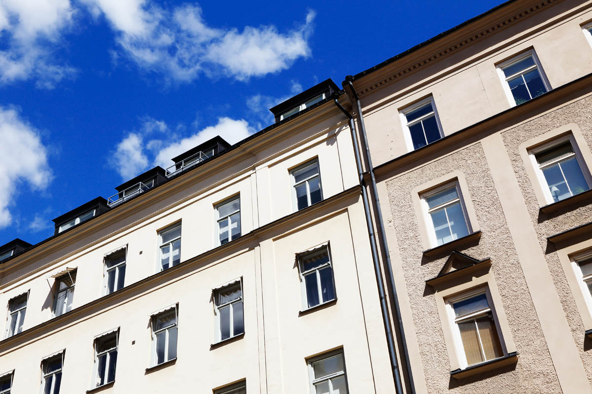 Flerbostadshus sett nerifrån med fasad och fönster mot blå himmel