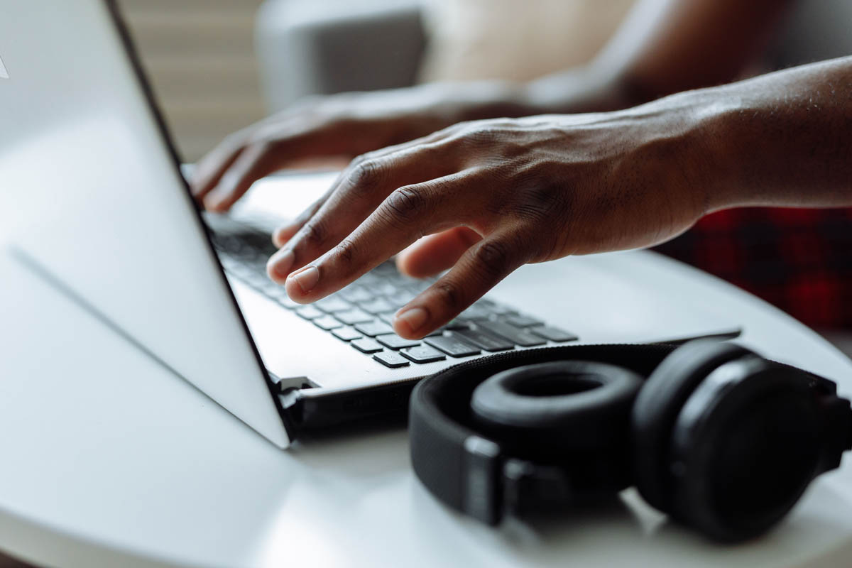 Händer som skriver på laptop på skrivbord med hörlurar bredvid